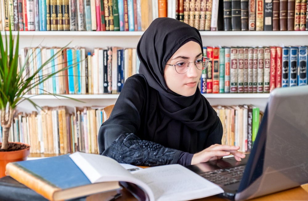 Studentin lernt mit Buch und Laptop in der Bibliothek